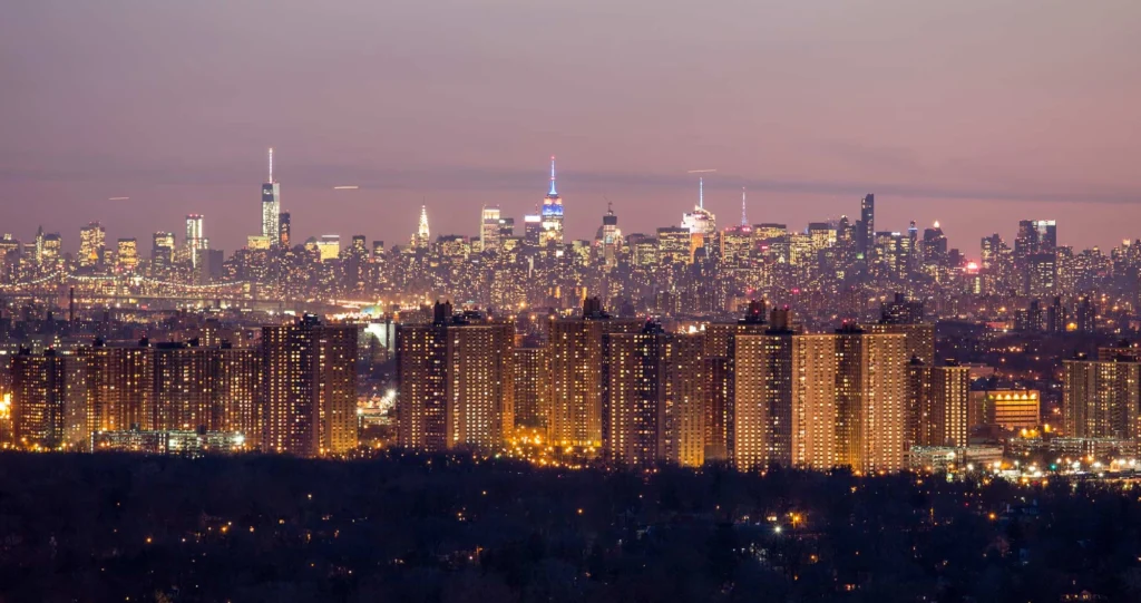 Panoramic view of New York City skyline at twilight with glowing apartment towers in foreground