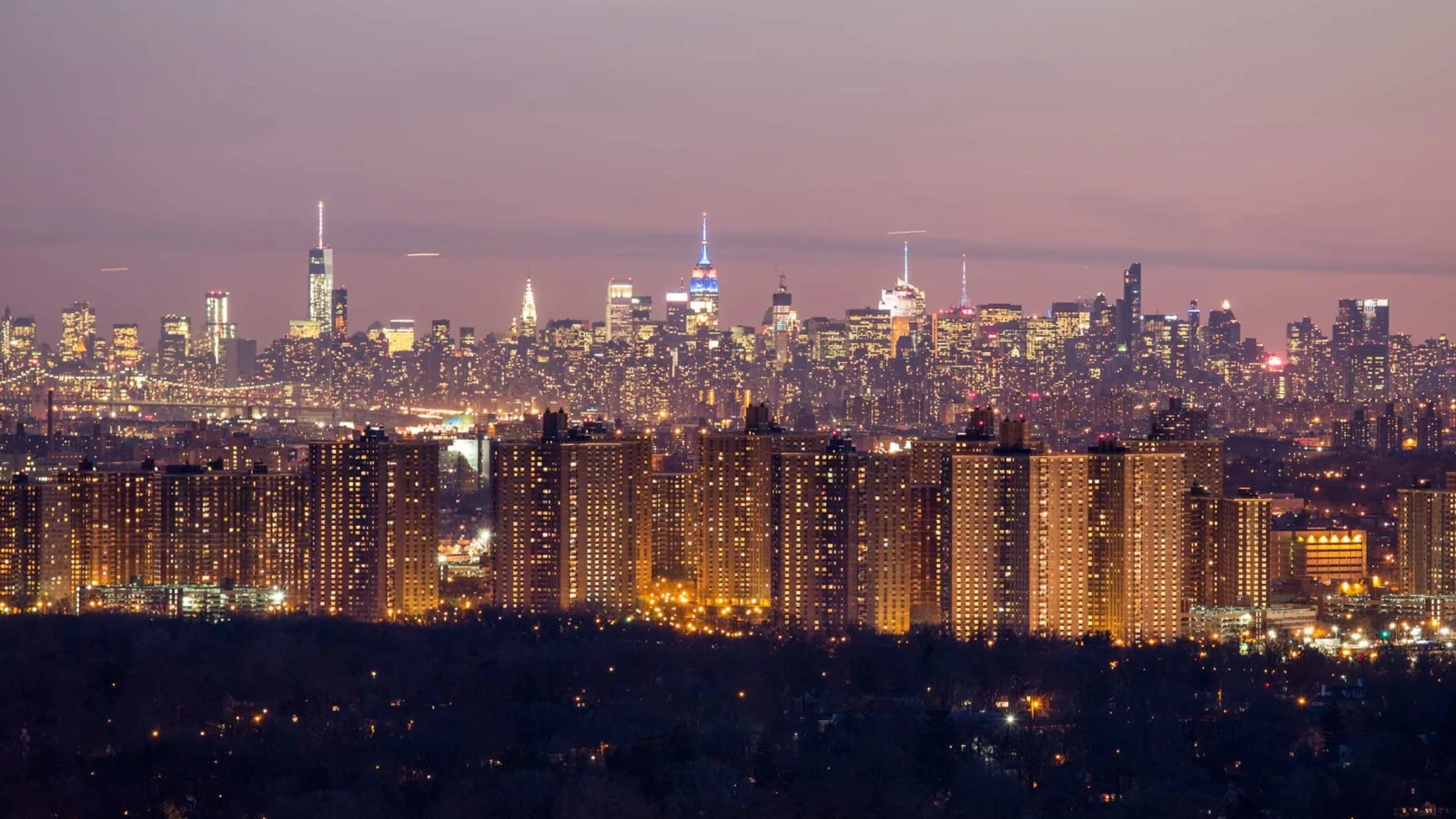 Panoramic view of New York City skyline at twilight with glowing apartment towers in foreground