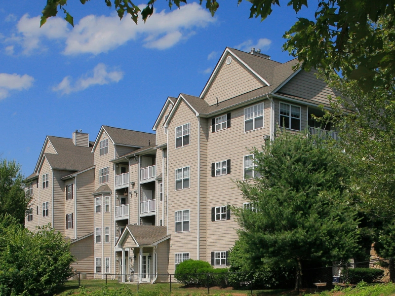 Garden-style beige apartment complex with gabled roofs surrounded by trees at Flanders Hill