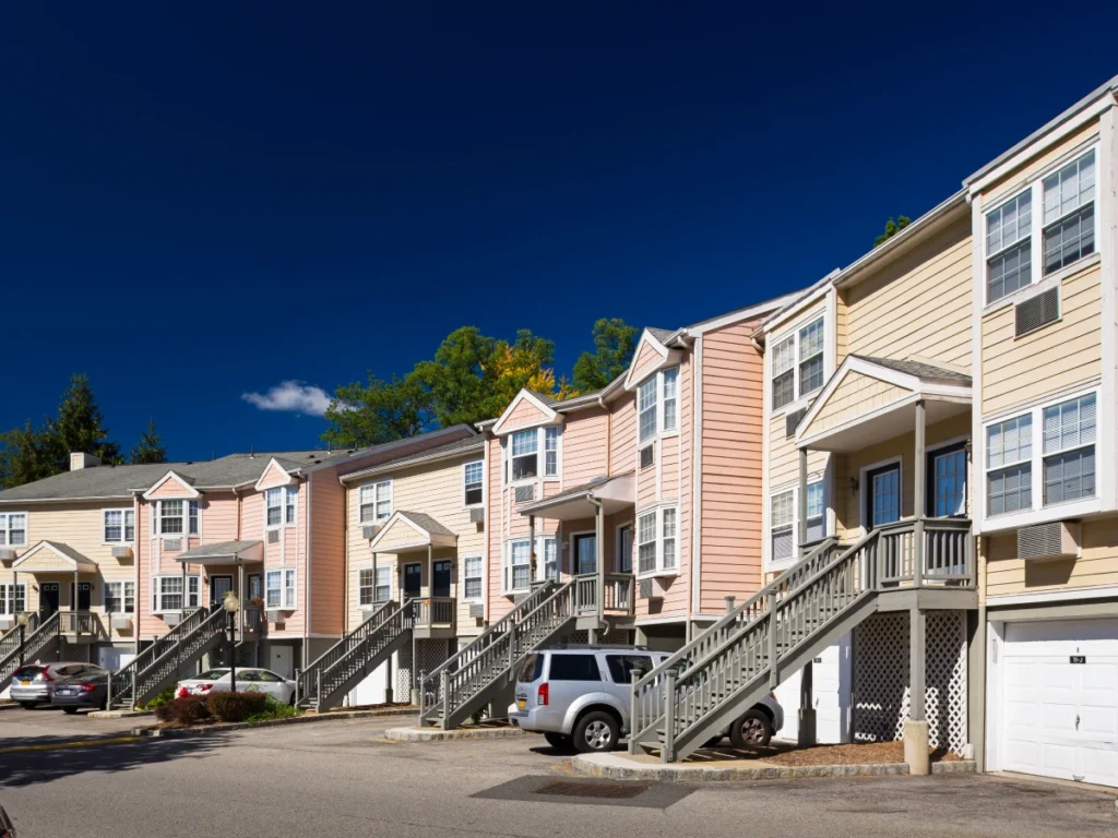 Townhouse-style apartment buildings with pastel color siding, raised porches, and parked vehicles