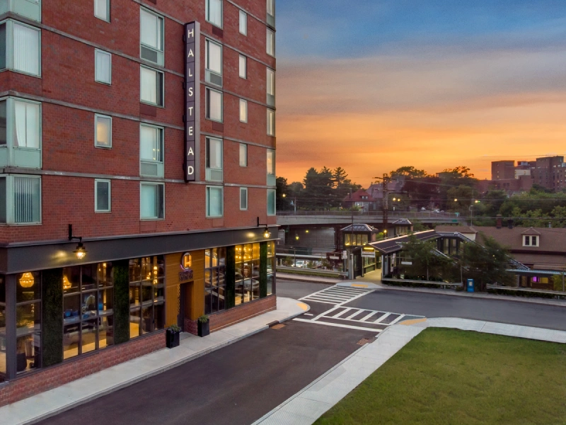Modern red-brick apartment building with Halstead signage and illuminated windows at sunset hour