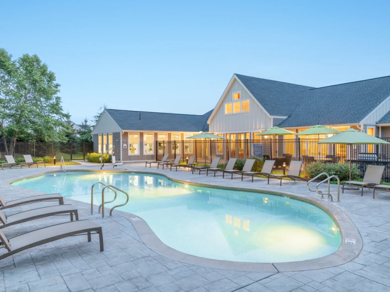 Resort-style pool area with lounge chairs and umbrellas beside a modern clubhouse building
