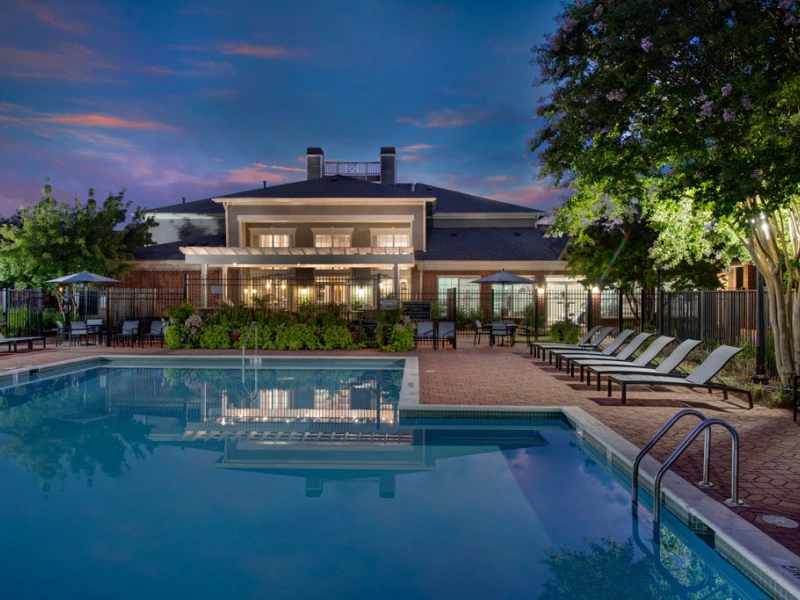Large community pool at dusk with clubhouse lighting reflecting on the water's surface