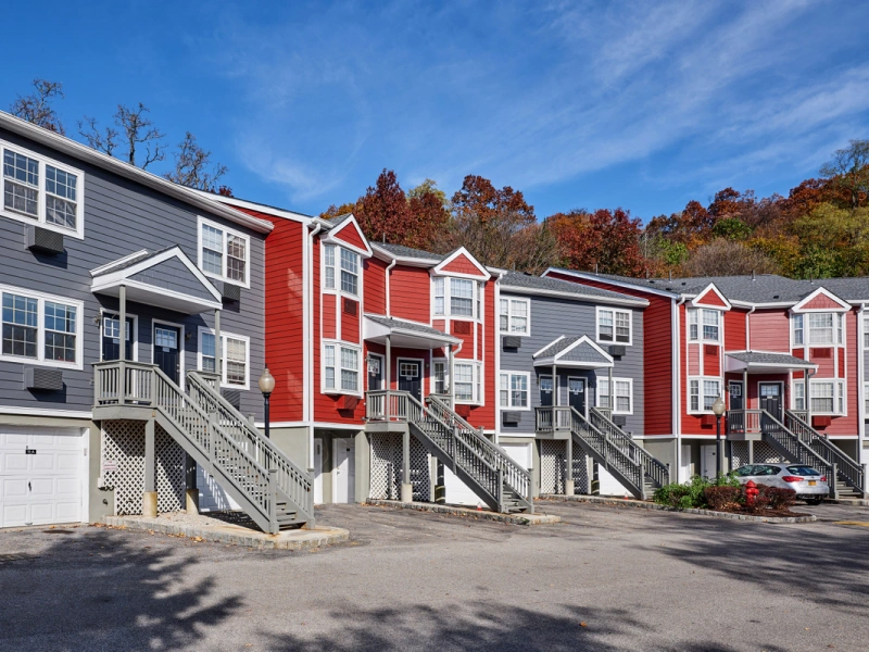 Multi-level residential townhomes with private staircases nestled against a wooded hillside backdrop
