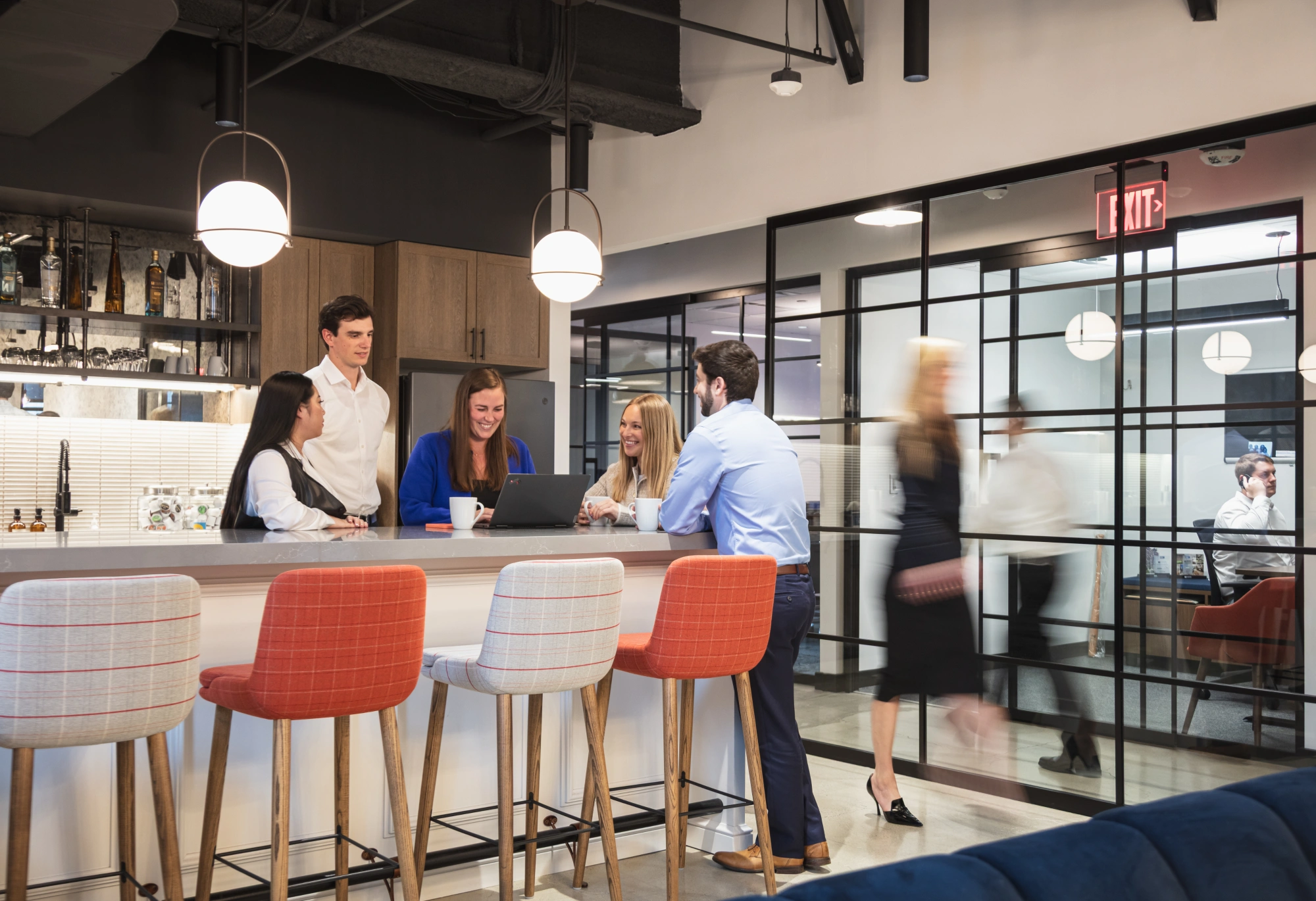 Group of young professionals smiling and collaborating around kitchen island in modern office space