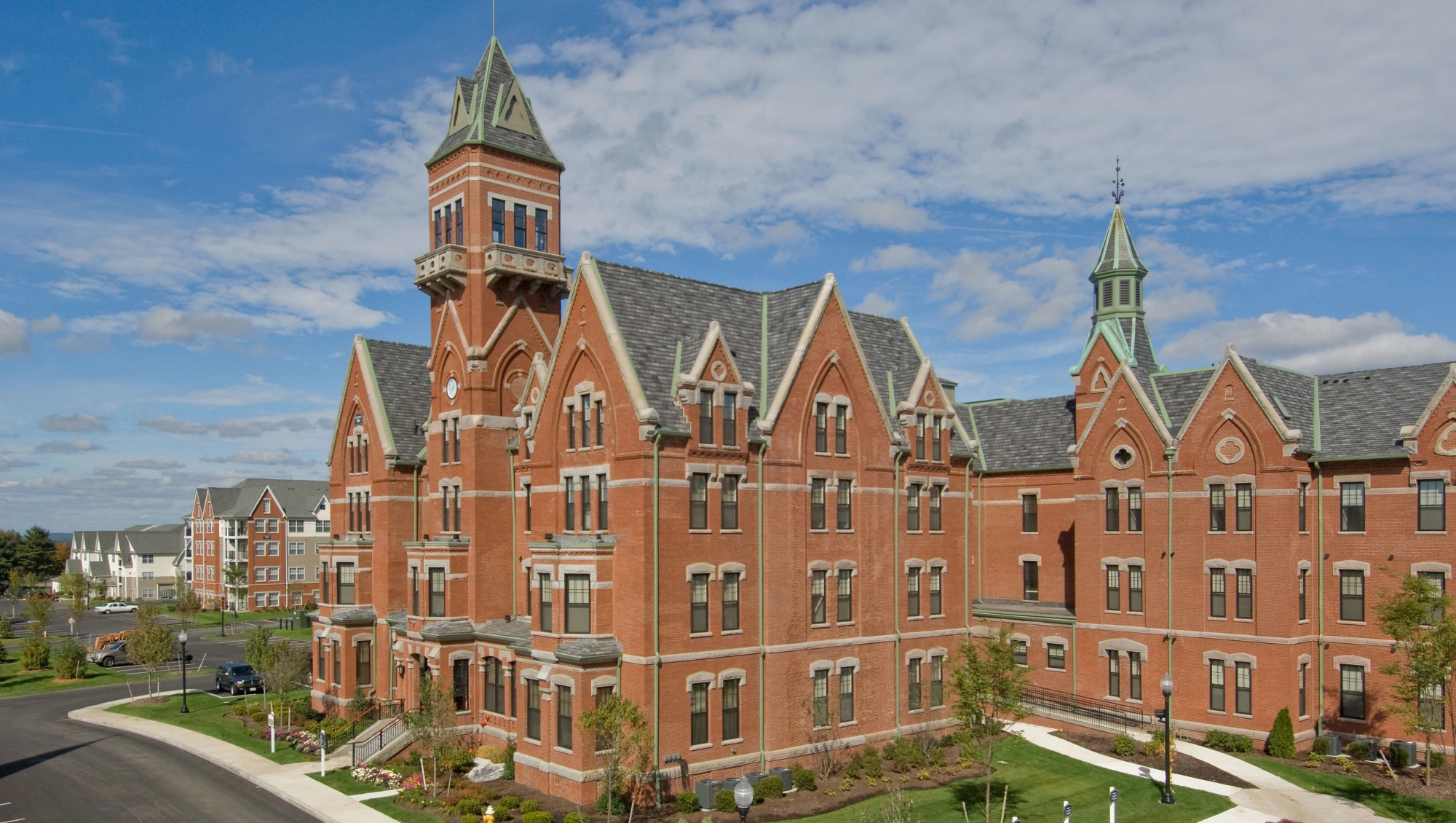 Historic red brick building with pointed towers under a bright blue sky with scattered clouds