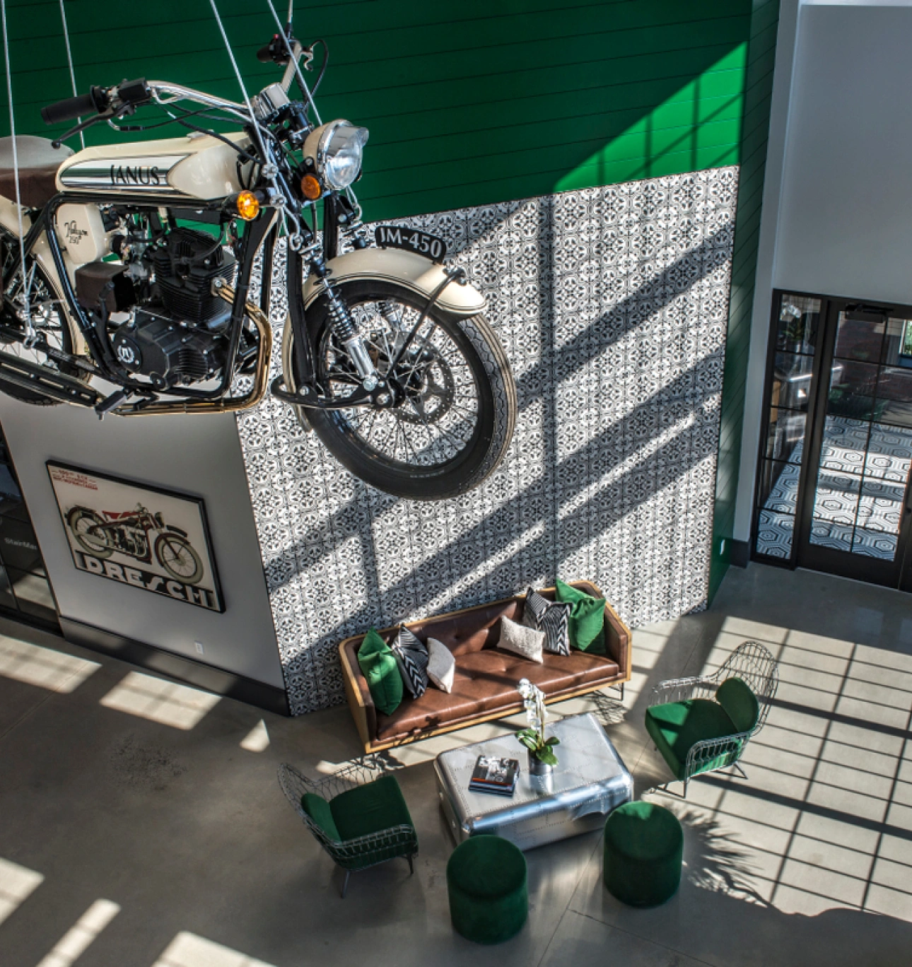 Vintage motorcycle suspended in eclectic interior lobby with green accent wall and modern furniture
