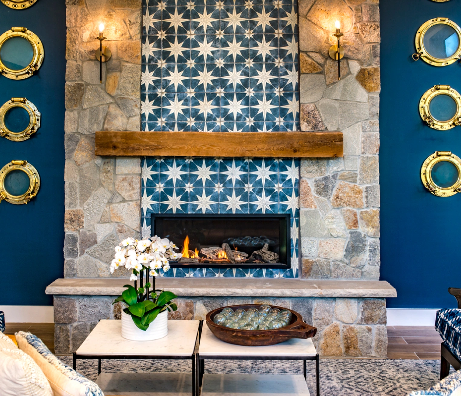 Nautical-themed lounge with stone fireplace, decorative tiles, and round brass-framed porthole mirrors