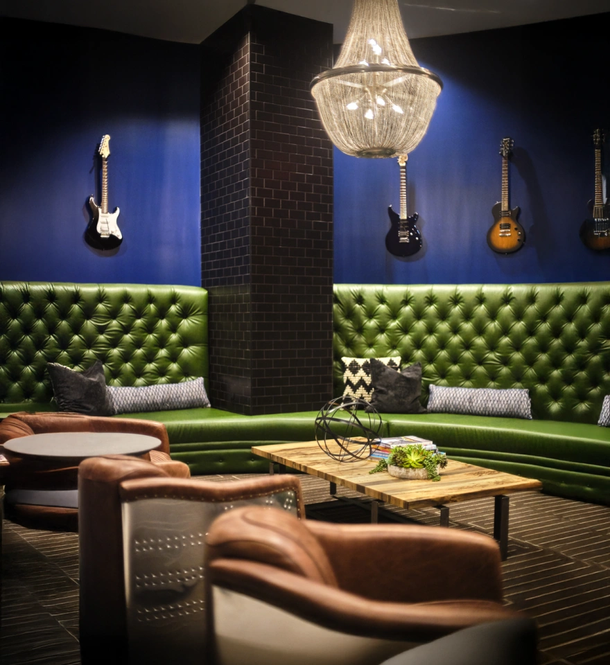 Lounge space featuring green tufted seating, hanging guitars, and cozy leather chairs