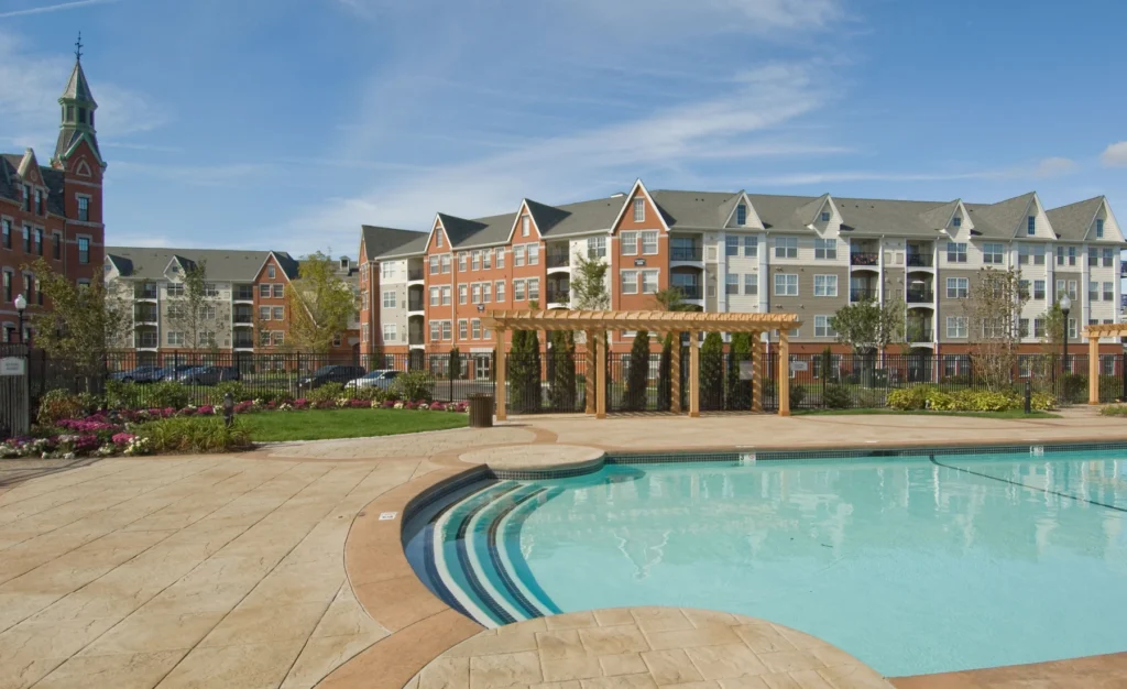 Luxury apartment complex with outdoor swimming pool, landscaped gardens, and sun deck seating area