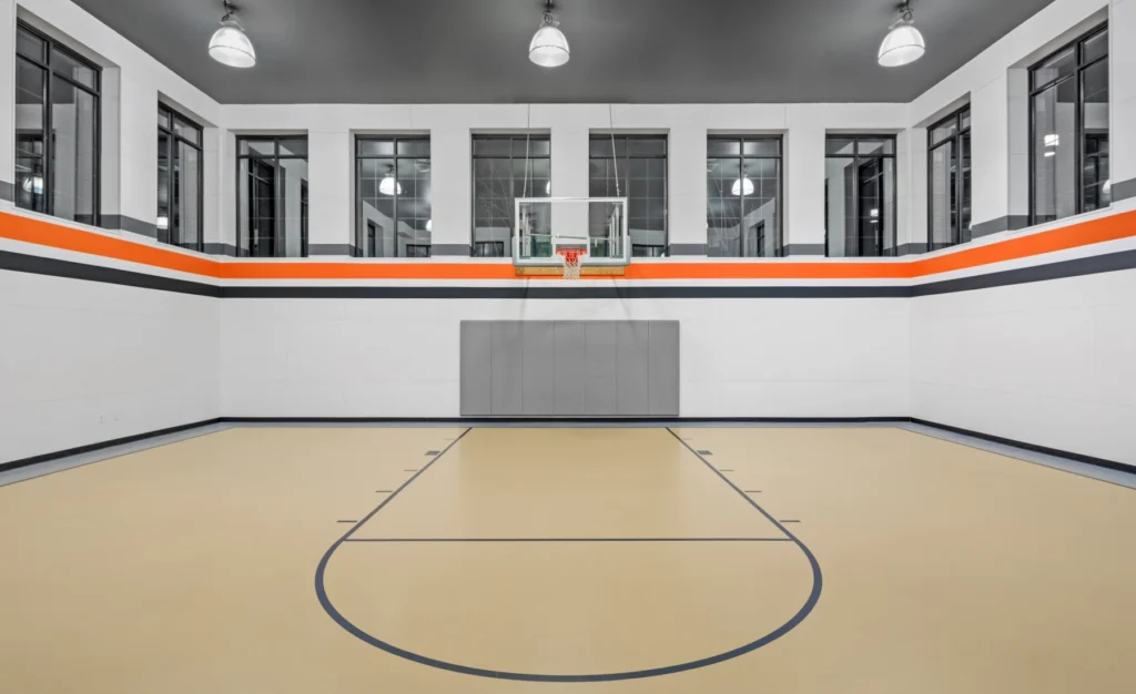 Indoor basketball court with light wood floor, high windows, and orange-striped white walls