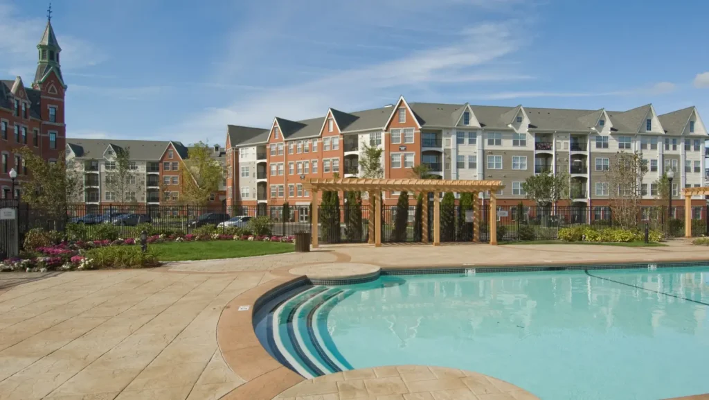 Luxury apartment complex with outdoor swimming pool, landscaped gardens, and sun deck seating area