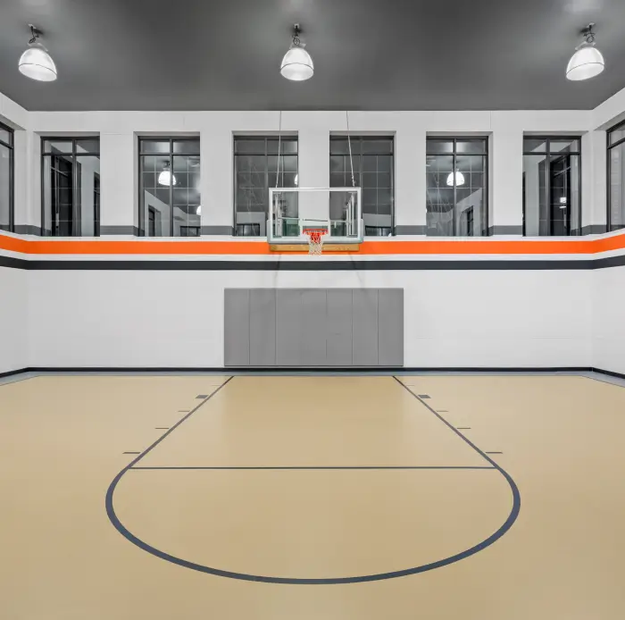 Indoor basketball court with light wood floor, high windows, and orange-striped white walls