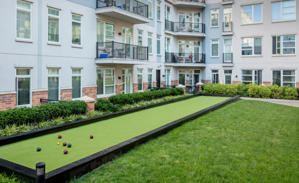 Residential bocce court on green lawn surrounded by shrubs and apartment balconies at Halstead Hoboken