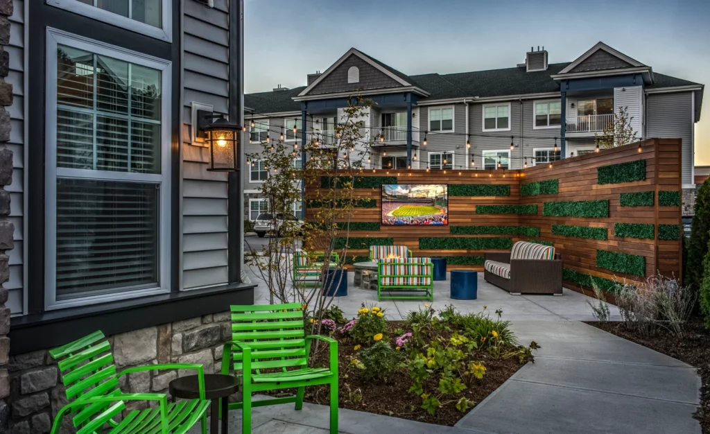 Cozy outdoor lounge space with green chairs, wood privacy wall, and string lights ambiance