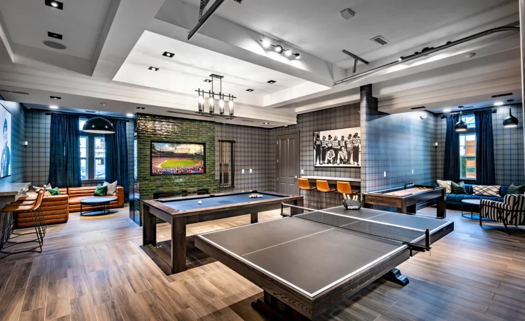 Game room with ping pong, pool tables, and lounge seating under decorative ceiling lights