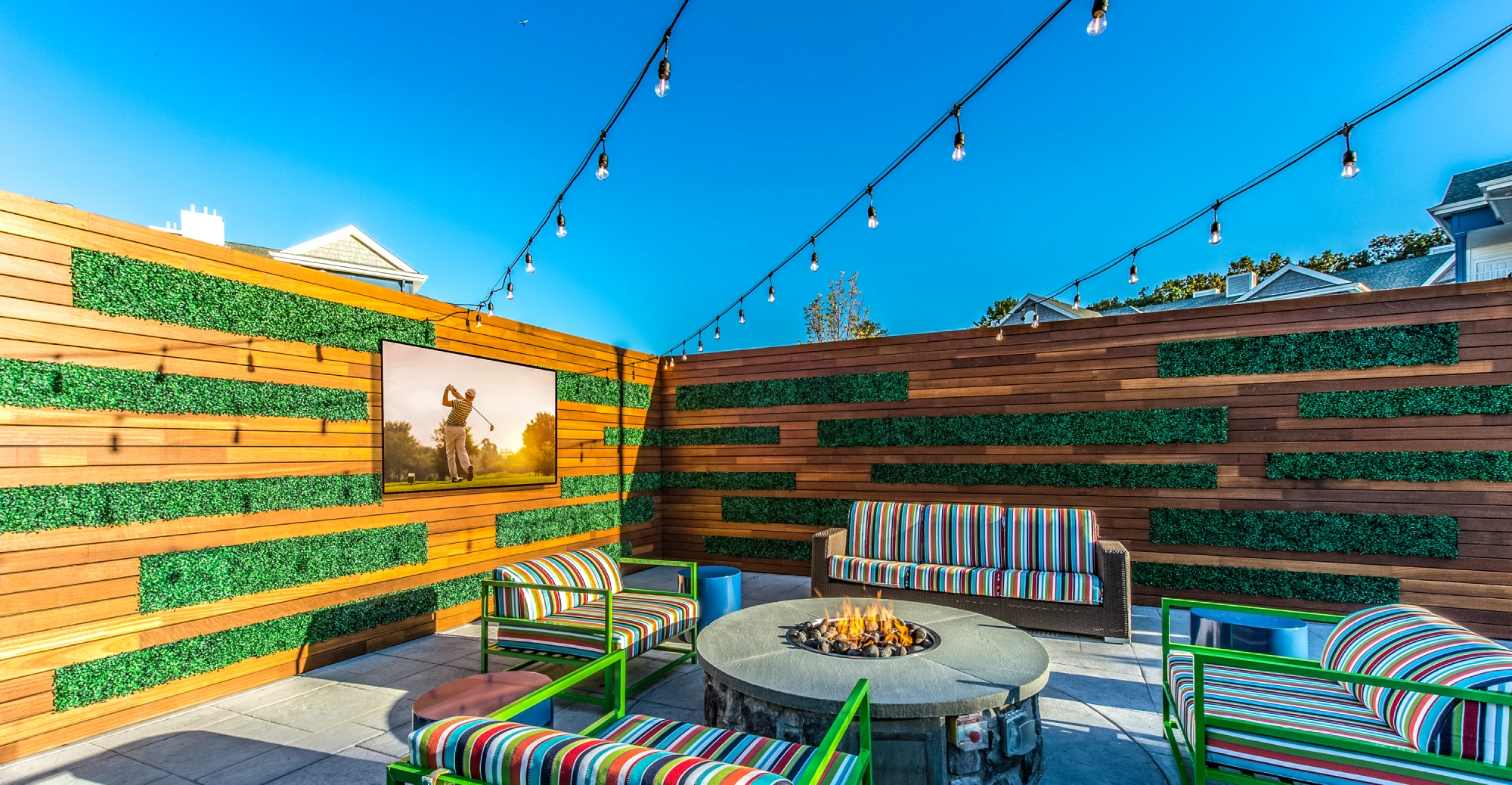 Outdoor lounge with striped furniture, fire pit, and hanging lights in Halstead Maynard Crossing
