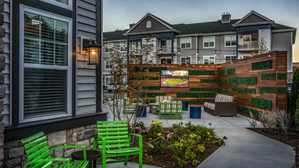 Cozy outdoor lounge space with green chairs, wood privacy wall, and string lights ambiance