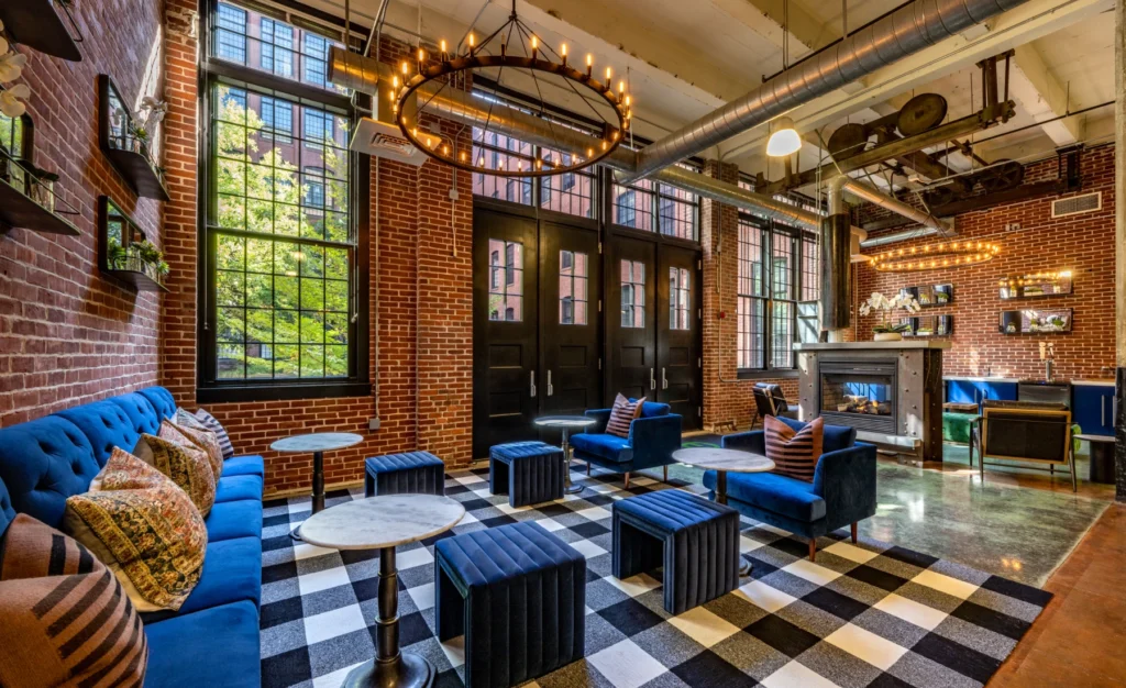 Industrial-style lounge in Halstead Providence with exposed brick, oversized windows, and bold blue velvet