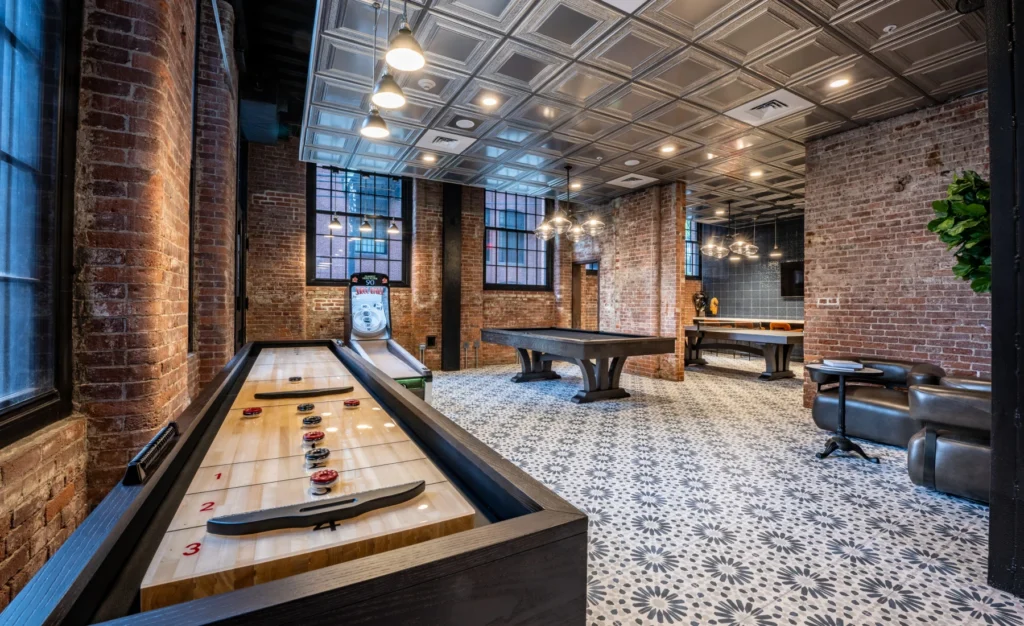 Industrial-style game room featuring shuffleboard, pool table, and exposed brick interior walls