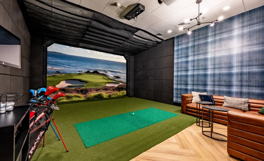 Indoor golf simulator with putting green, leather seating, and realistic oceanfront course display
