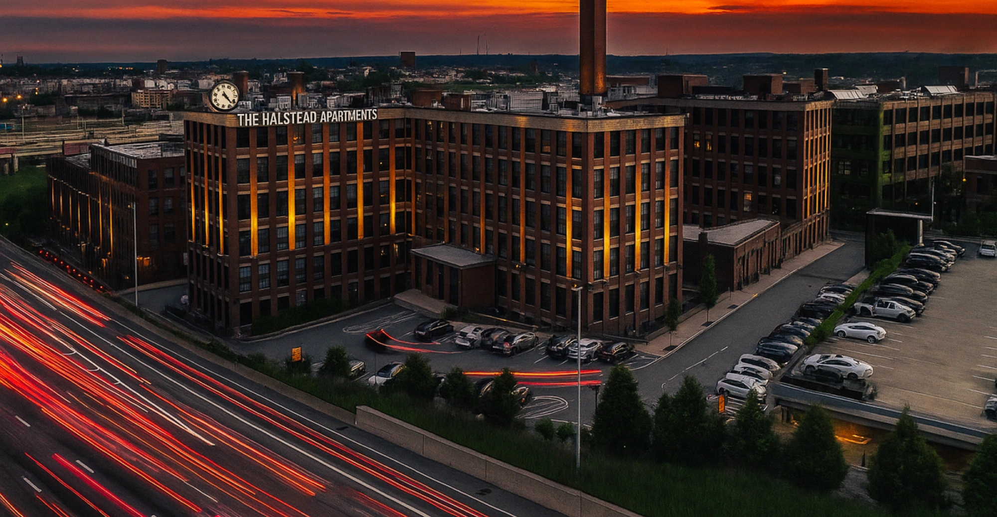Aerial twilight view of Halstead Providence Apartments with glowing lights and highway light trails