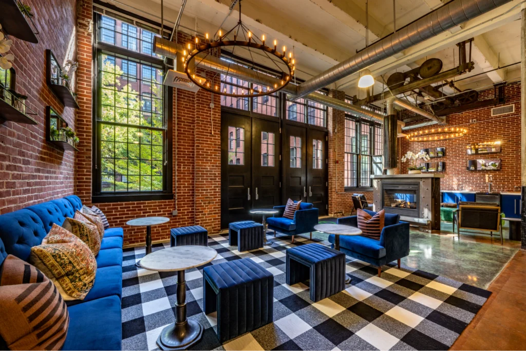 Industrial-style lounge in Halstead Providence with exposed brick, oversized windows, and bold blue velvet