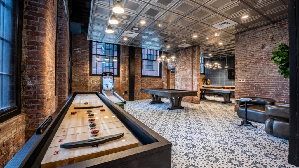 Industrial-style game room featuring shuffleboard, pool table, and exposed brick interior walls