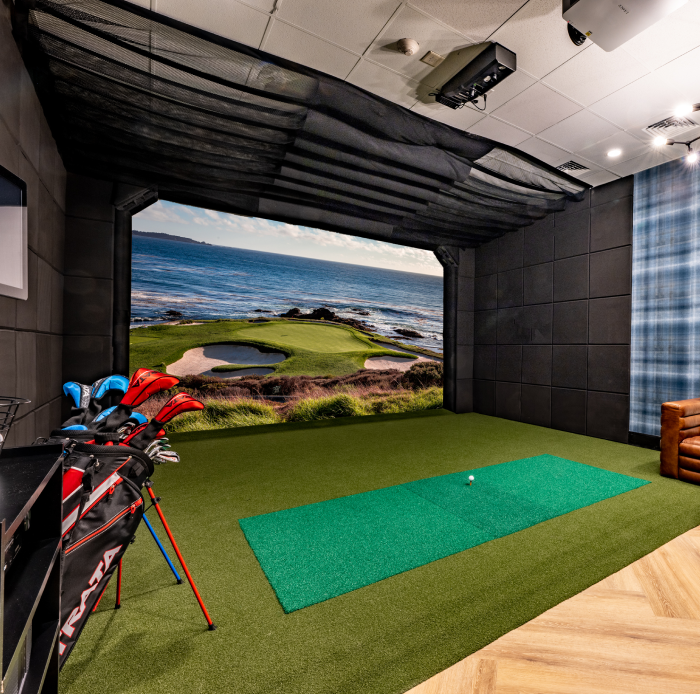 Indoor golf simulator with putting green, leather seating, and realistic oceanfront course display