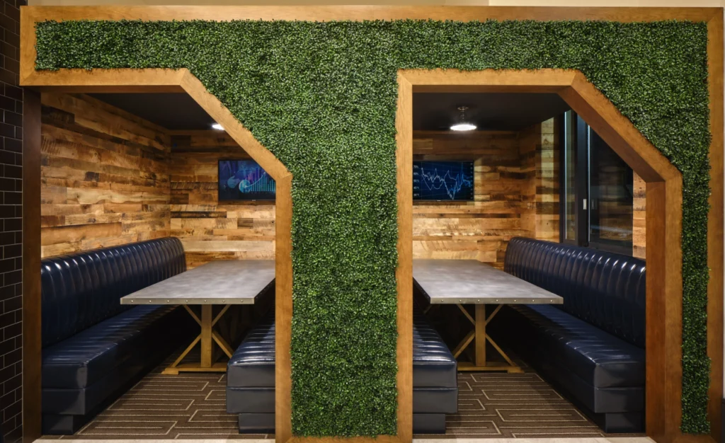 Cozy booth seating areas with wooden walls, industrial lighting, and artificial greenery divider