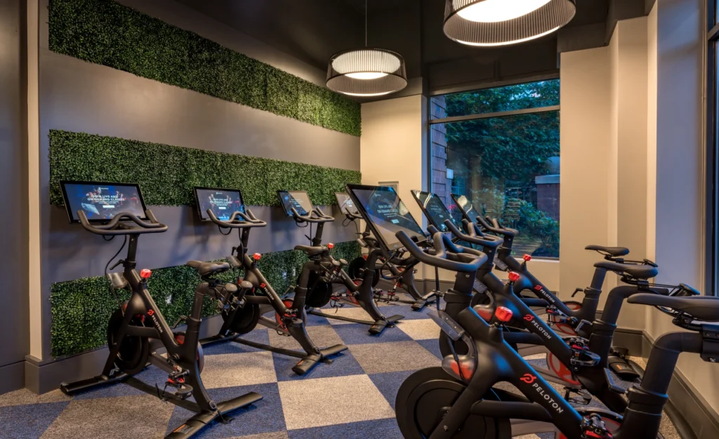 Indoor Peloton cycling studio with multiple bikes, greenery-accented wall, and natural light